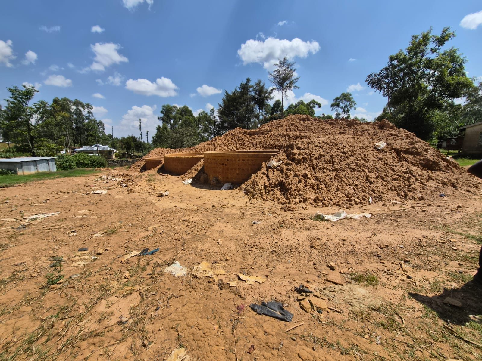 Brick-lined mining pit walls beneath a large heap of excavated soil, with litter scattered on bare ground